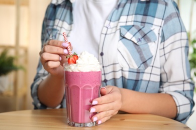 Woman holding tasty fresh milk shake with strawberry at table indoors, closeup