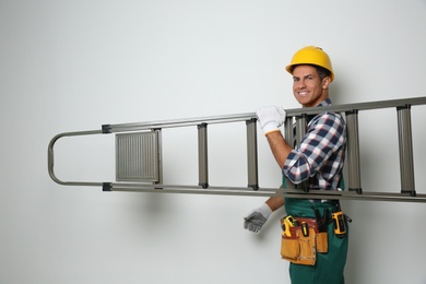 Professional builder carrying metal ladder on light background