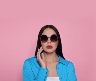 Attractive serious woman in fashionable sunglasses against pink background