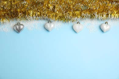 Shiny golden tinsel, Christmas baubles and snow on light blue background, flat lay. Space for text