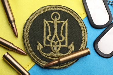 Bullets, ID tags and military patch on Ukrainian flag, flat lay