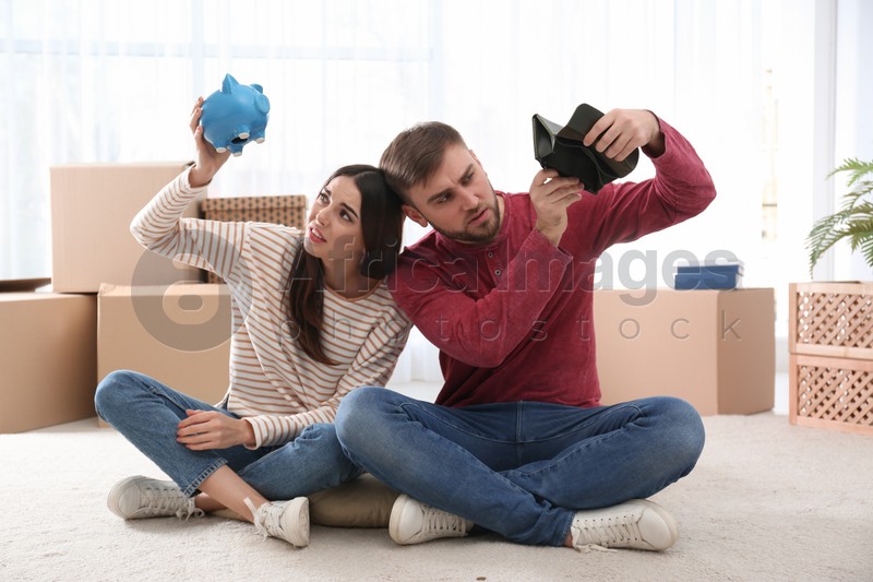Unhappy young couple with empty piggy bank and wallet at home. Money problems