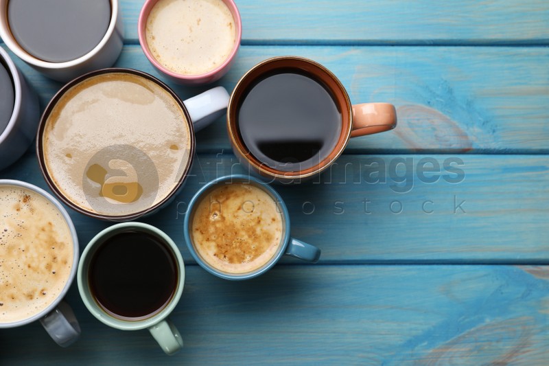 Photo of Many cups of different coffee drinks on light blue wooden table, flat lay. Space for text