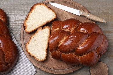 Cut homemade braided bread and knife on wooden table, flat lay. Challah for Shabbat