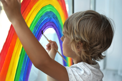 Little boy drawing rainbow on window. Stay at home concept