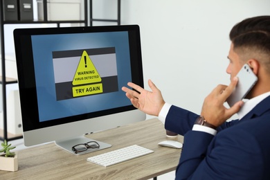Office worker in front of computer with warning about virus attack on screen