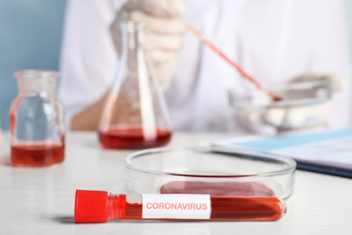 Test tube with blood sample and label CORONA VIRUS and Petri dish on table in laboratory, closeup