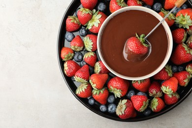 Photo of Fondue fork with strawberry in bowl of melted chocolate surrounded by different berries on light table, top view