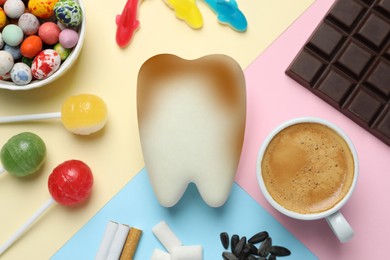 Decayed tooth model and harmful for enamel products on color background, flat lay