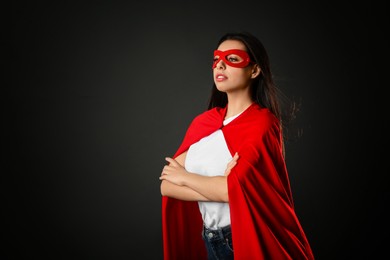 Confident young woman wearing superhero cape and mask on grey background, space for text