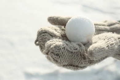 Woman in knitted mittens holding snowball outdoors, closeup