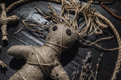 Female voodoo doll with pins surrounded by ceremonial items on black wooden background, closeup