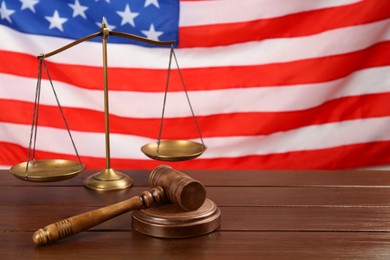 Scales of justice and gavel on wooden table against American flag. Space for text