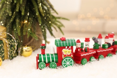 Bright toy train on artificial snow near small Christmas tree