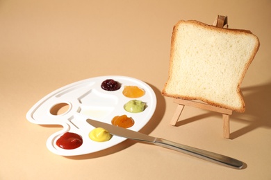 Slice of bread on small easel and palette with different sauces against beige background