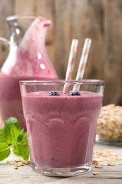 Glass of blackberry smoothie with straws, mint and oatmeal on light wooden table