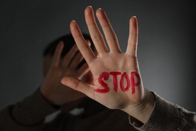 Photo of Woman with word Stop written on hand against black background, closeup. Domestic violence concept