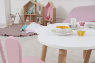 Photo of Toy tableware on white table in playroom. Interior design