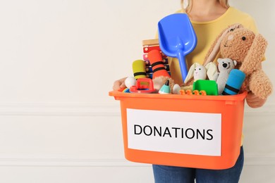 Woman holding donation box with child toys against light background, closeup. Space for text