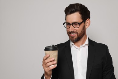 Handsome bearded man with glasses looking at paper cup on light grey background. Space for text