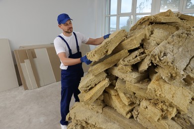 Construction worker with used glass wool in room prepared for renovation