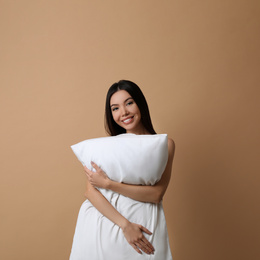 Beautiful Asian woman with pillow on beige background. Bedtime