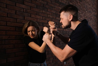 Man abusing scared woman near brick wall. Domestic violence