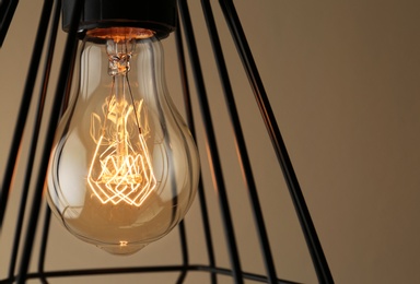 Photo of Hanging lamp bulb in chandelier against beige background, closeup
