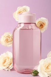 Bottle of micellar water and beautiful roses on light pink background