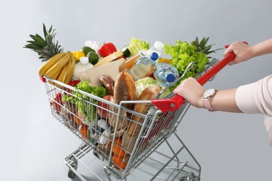 Woman with shopping cart full of groceries on grey background, closeup