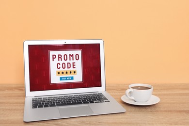 Laptop with activated promo code on wooden table near beige wall