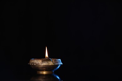 Photo of Lit diya on black background, space for text. Diwali lamp