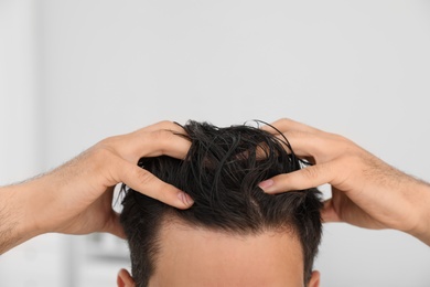 Man applying hair conditioner against light background, closeup