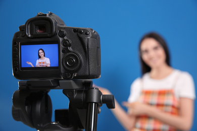 Young blogger recording video against blue background, focus on camera screen