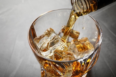 Pouring whiskey from bottle into glass with ice cubes on table, closeup