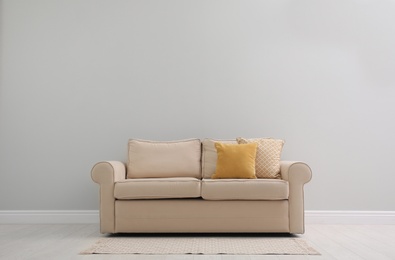 Comfortable beige sofa near light wall indoors, space for text. Simple interior