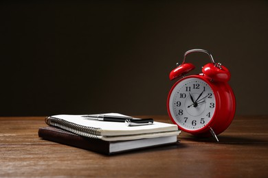 Alarm clock and office stationery on wooden table against dark background, space for text. Time management