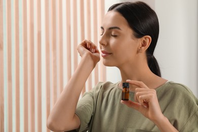 Photo of Young woman smelling essential oil on wrist indoors