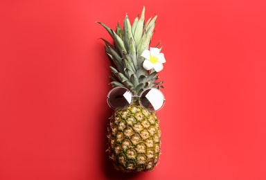 Photo of Pineapple with sunglasses and plumeria flower on red background, top view. Creative concept