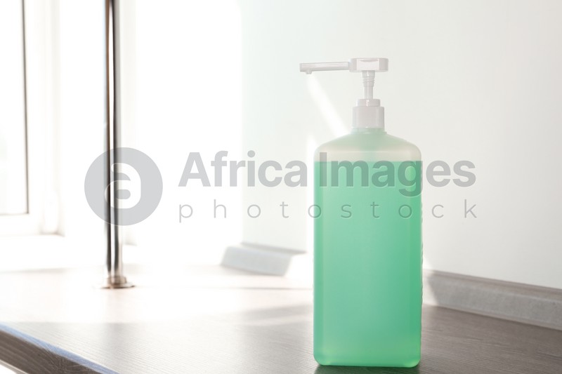 Dispenser bottle with green antiseptic gel on wooden shelf indoors. Space for text