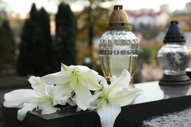 White lilies and grave lights on granite tombstone outdoors. Funeral ceremony