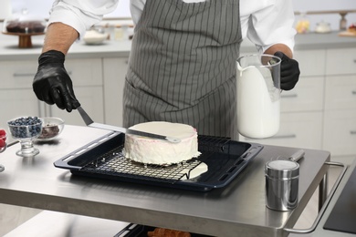 Male pastry chef preparing cake at table in kitchen, closeup