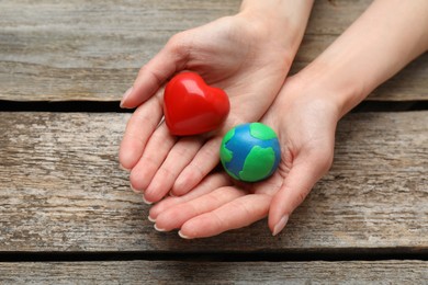 Happy Earth Day. Woman with plasticine planet and decorative heart at wooden table, closeup