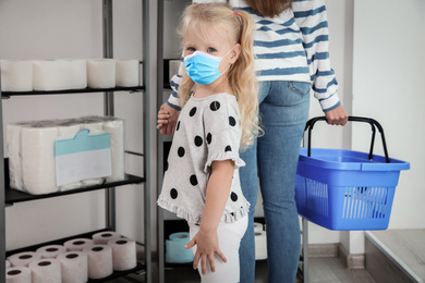 Little girl with medical mask and mother buying toilet paper in shop