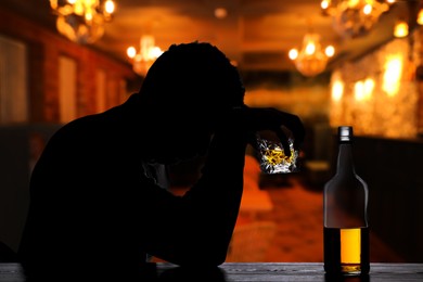 Silhouette of addicted man with alcoholic drink in bar