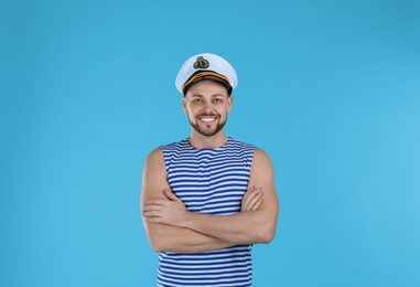 Happy sailor wearing cap on light blue background
