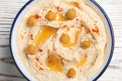Bowl of tasty hummus with chickpeas and paprika on white wooden table, top view