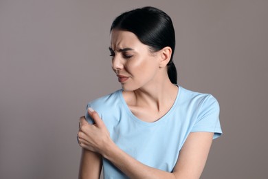 Woman suffering from shoulder pain on beige background
