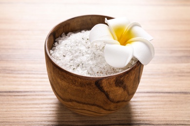 White sea salt for spa scrubbing procedure and flower on wooden table
