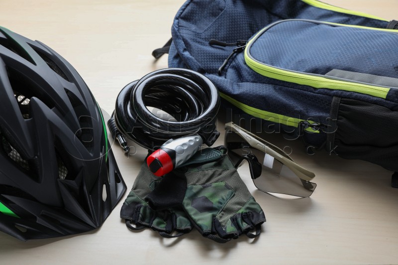 Photo of Bicycle cable lock, sunglasses, helmet and fingerless gloves near backpack on wooden table